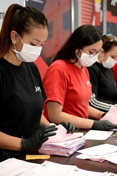 Personas con mascarilla y guantes organizando hojas de papel en un escritorio